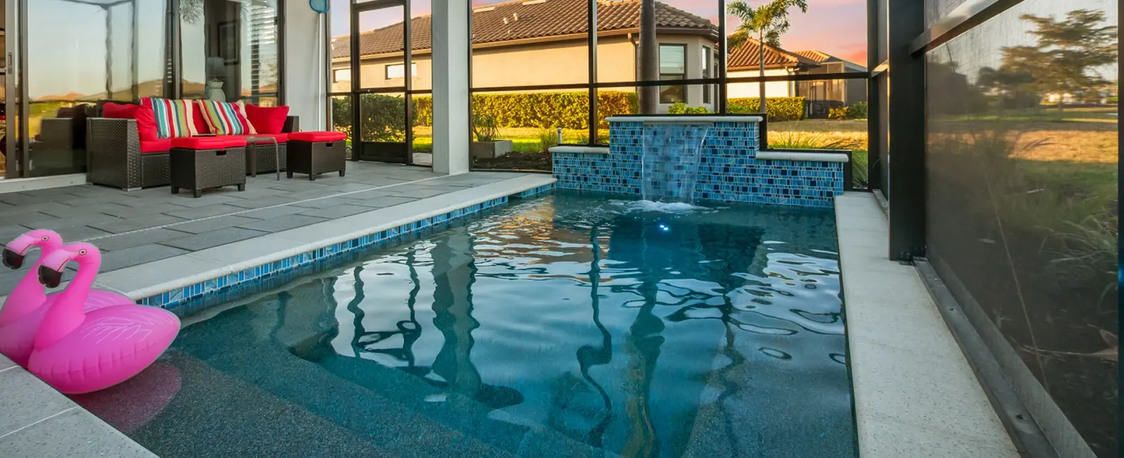 Screened lanai pool with a raised spa and glass-tile waterfall spillway at dusk.
